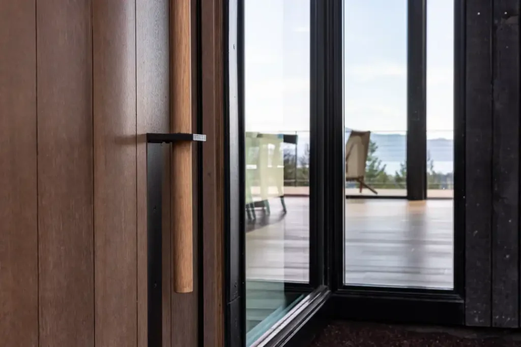 Wood front door with a dark metal handle at Basking Moose, beside corner windows framing the deck and Lake Pend Oreille beyond.