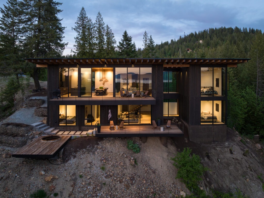 Basking Moose at The Idaho Club, built by Smithwright, with dark siding, expansive windows, and two levels of decks on a wooded hillside at dusk.